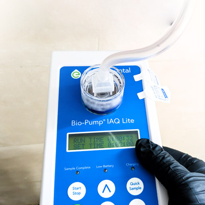 A mold inspector performing wall cavity air sampling by drilling a small hole to test for hidden mold growth behind drywall.